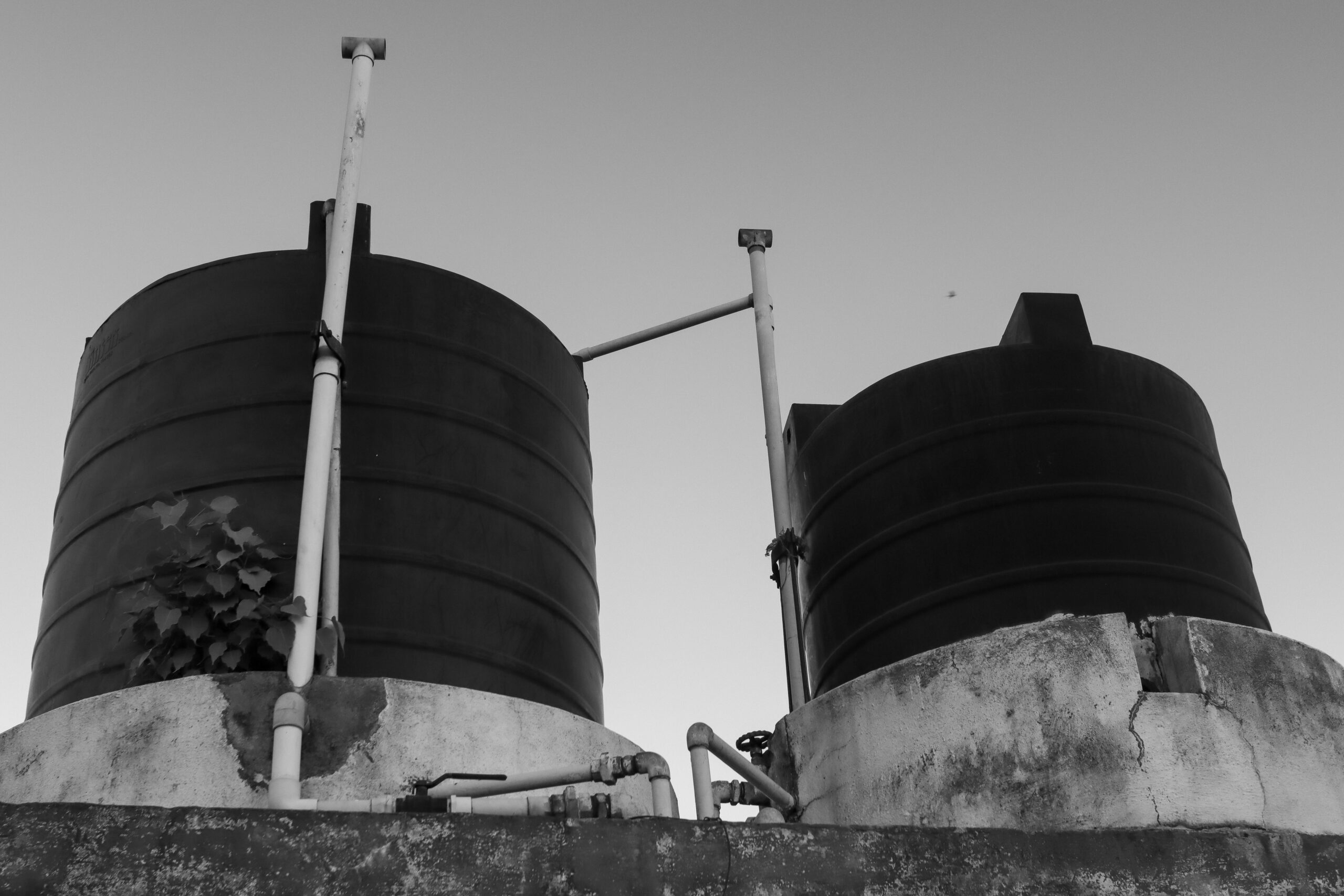 Two large cylindrical water storage tanks connected by metal pipes atop a concrete platform, seen in black and white.
